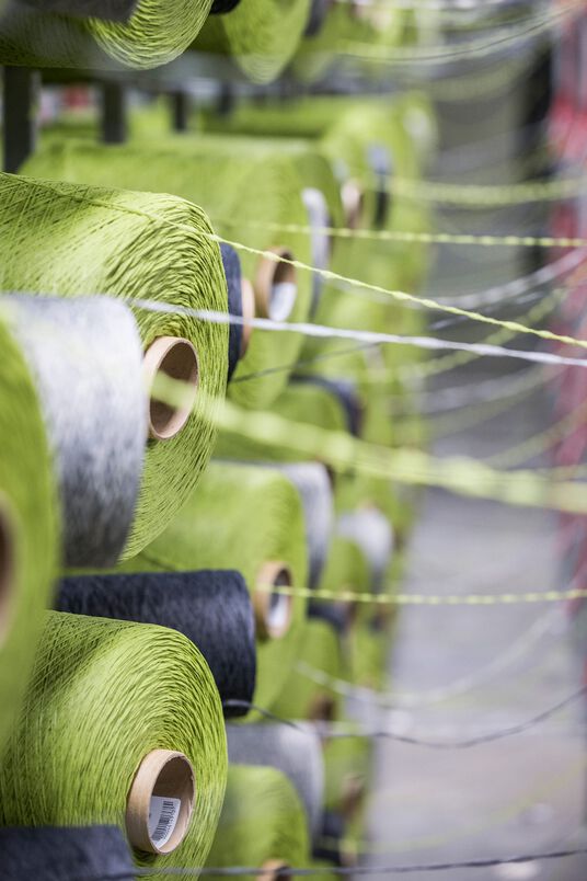 Close view of industrial skeins of green, gray, and white carpet tile threads.